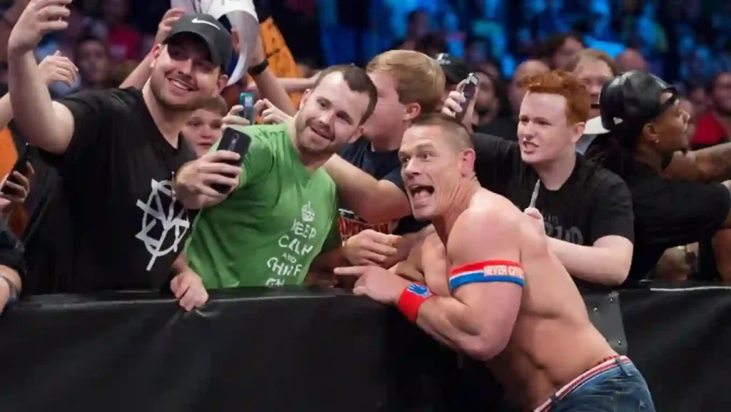 John Cena smiling and taking picture with a group of fans, ringside